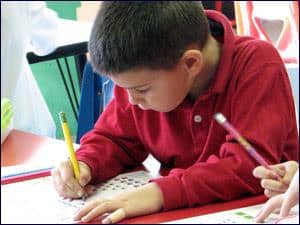 A young student focused on writing in a classroom setting at St. Joan of Arc Catholic School.